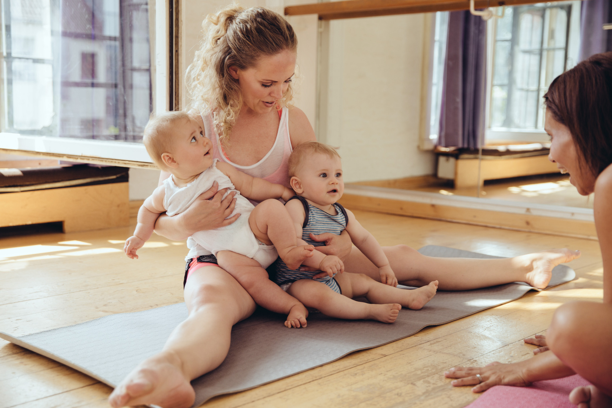 Mother with twin babies sitting on yoga mat, Cologne, NRW, Germany