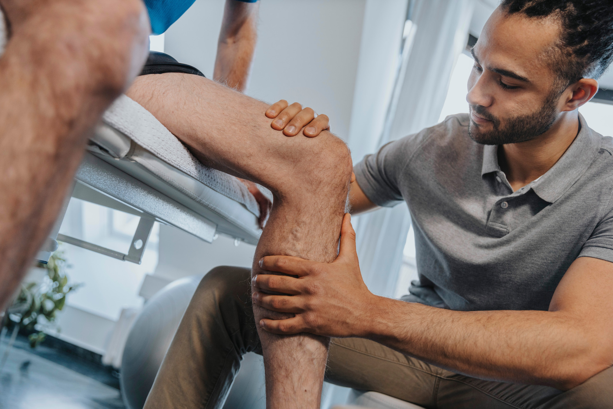 Physiotherapist touching knee of patient in practice, Cologne, NRW, Germany