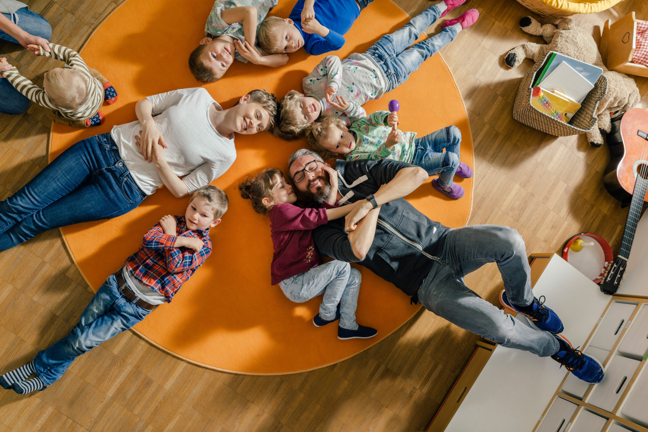 Children and teachers laying on carpet in Daycare center, Pre-school or Kindergarten, Cologne, NRW, Germany