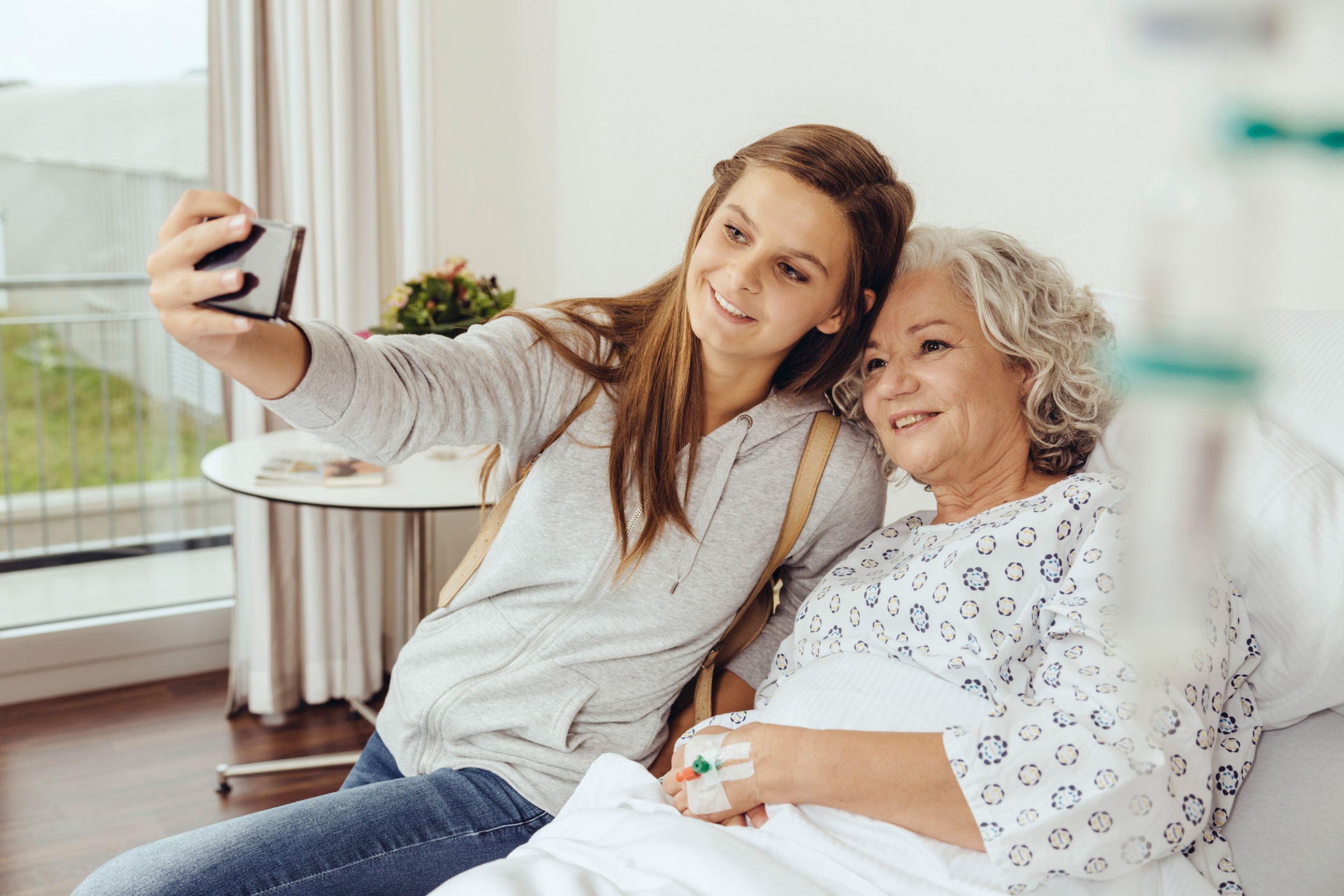Young woman visiting her grandmother in hospital, taking a selfie or videochatting