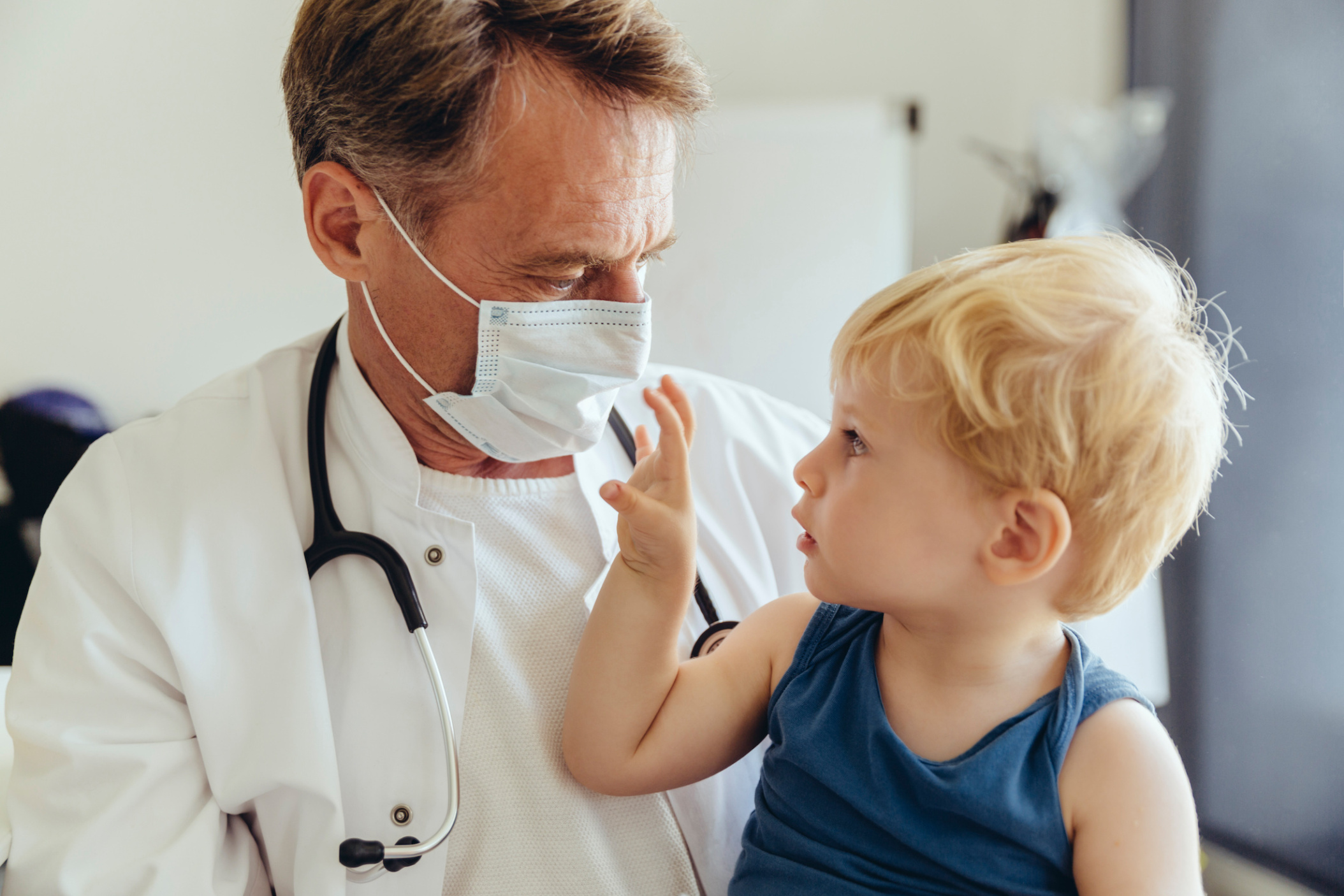 Doctor wearing a surgical mask while talking to curious infant patient, Germany