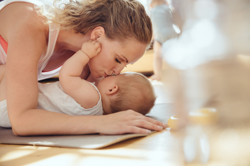 Mother kissing her baby while working out on a yoga mat, Cologne, NRW, Germany