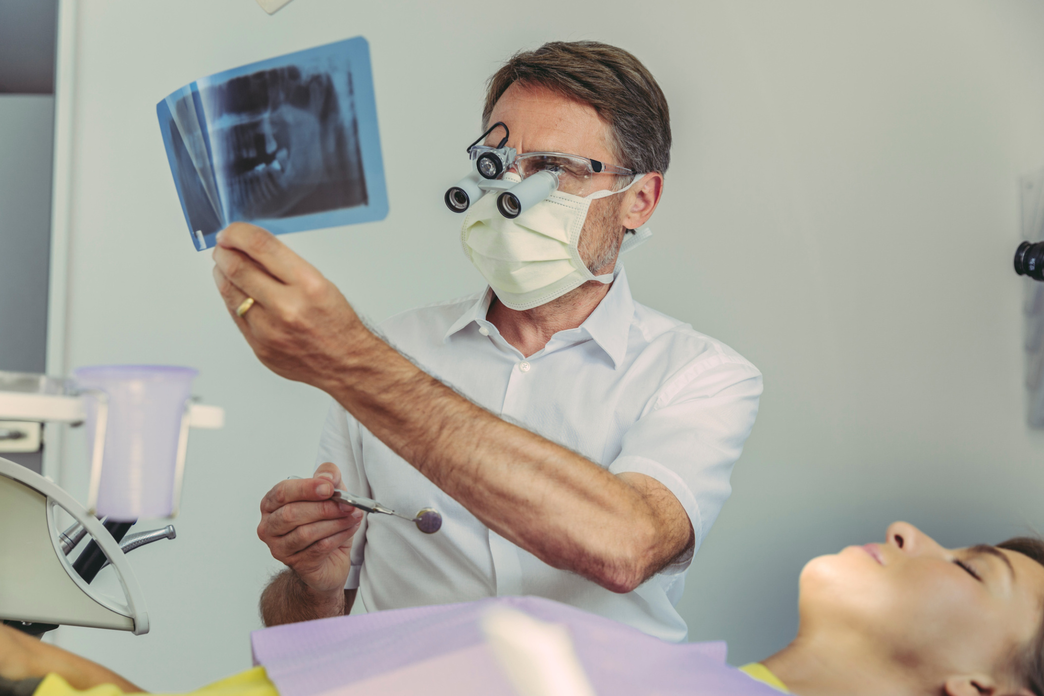 Male dentist holding up an x-ray image of a set of teeth before working on his patient, Germany