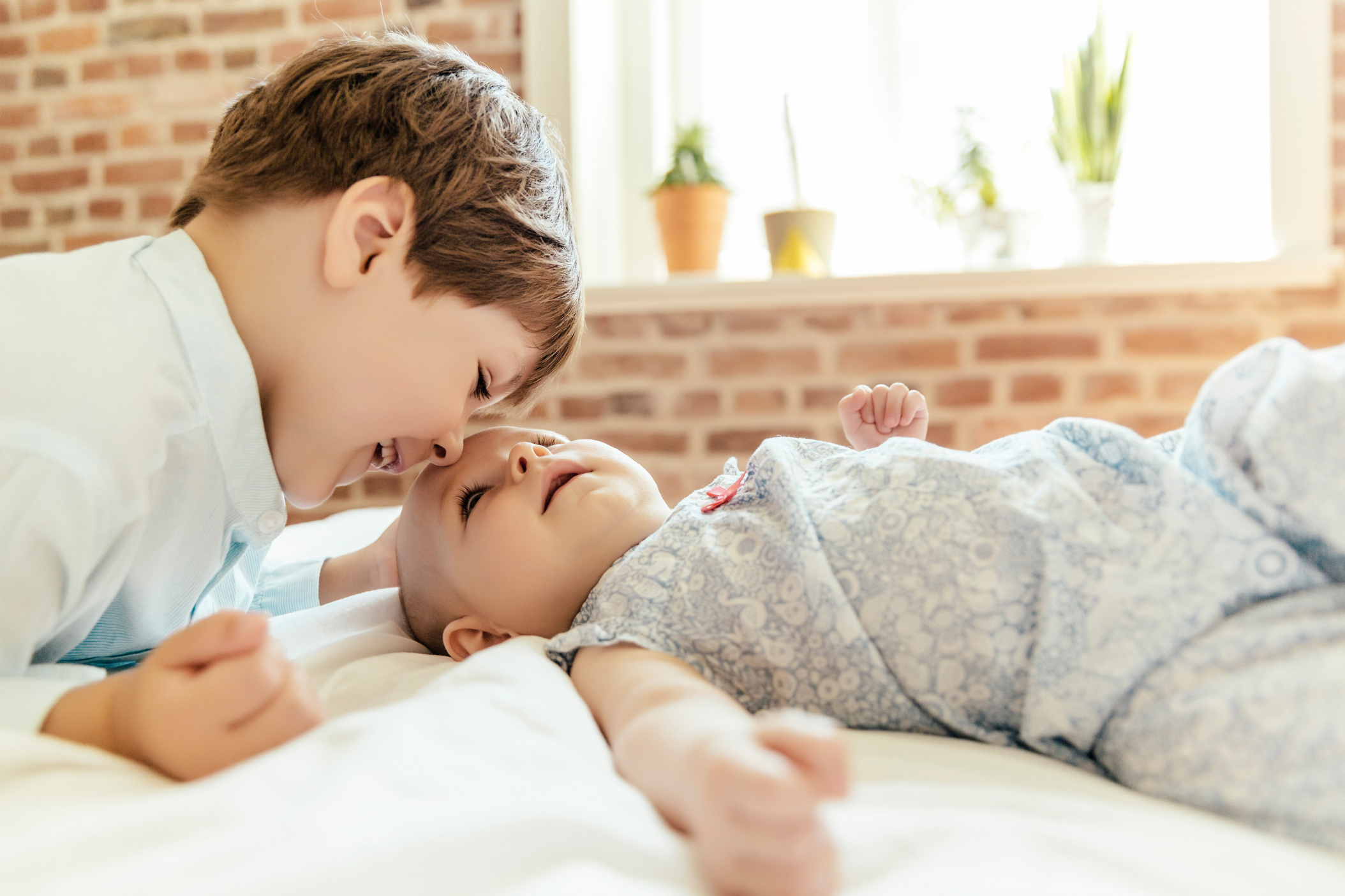 Brother cuddling and talking with his baby sister on bed