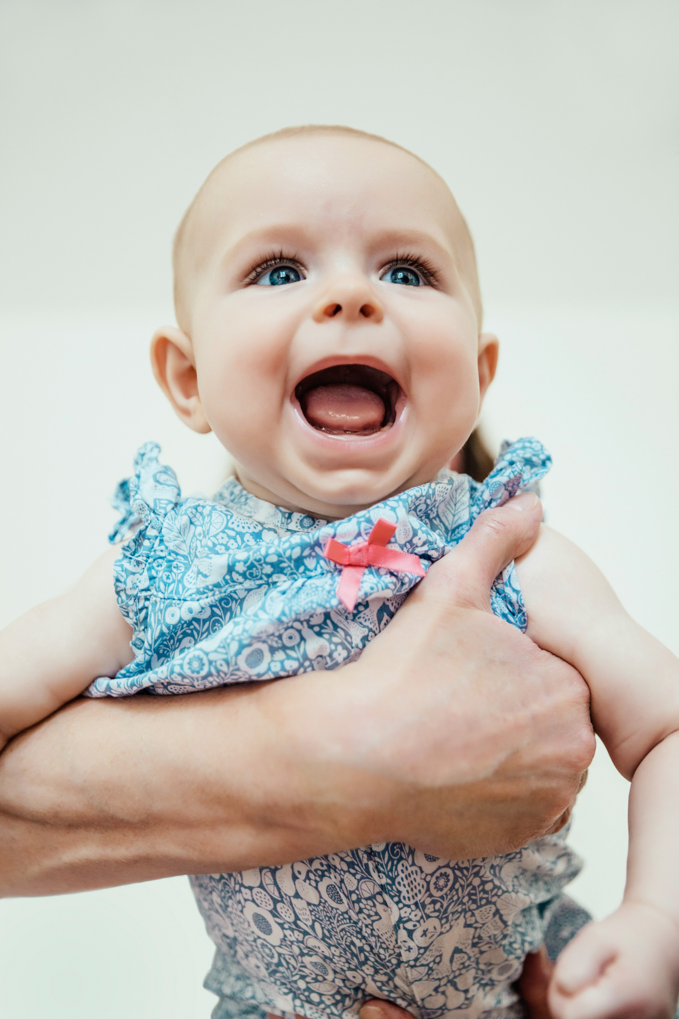 Laughing baby girl (4-8 months old) being held up by parent’s arm