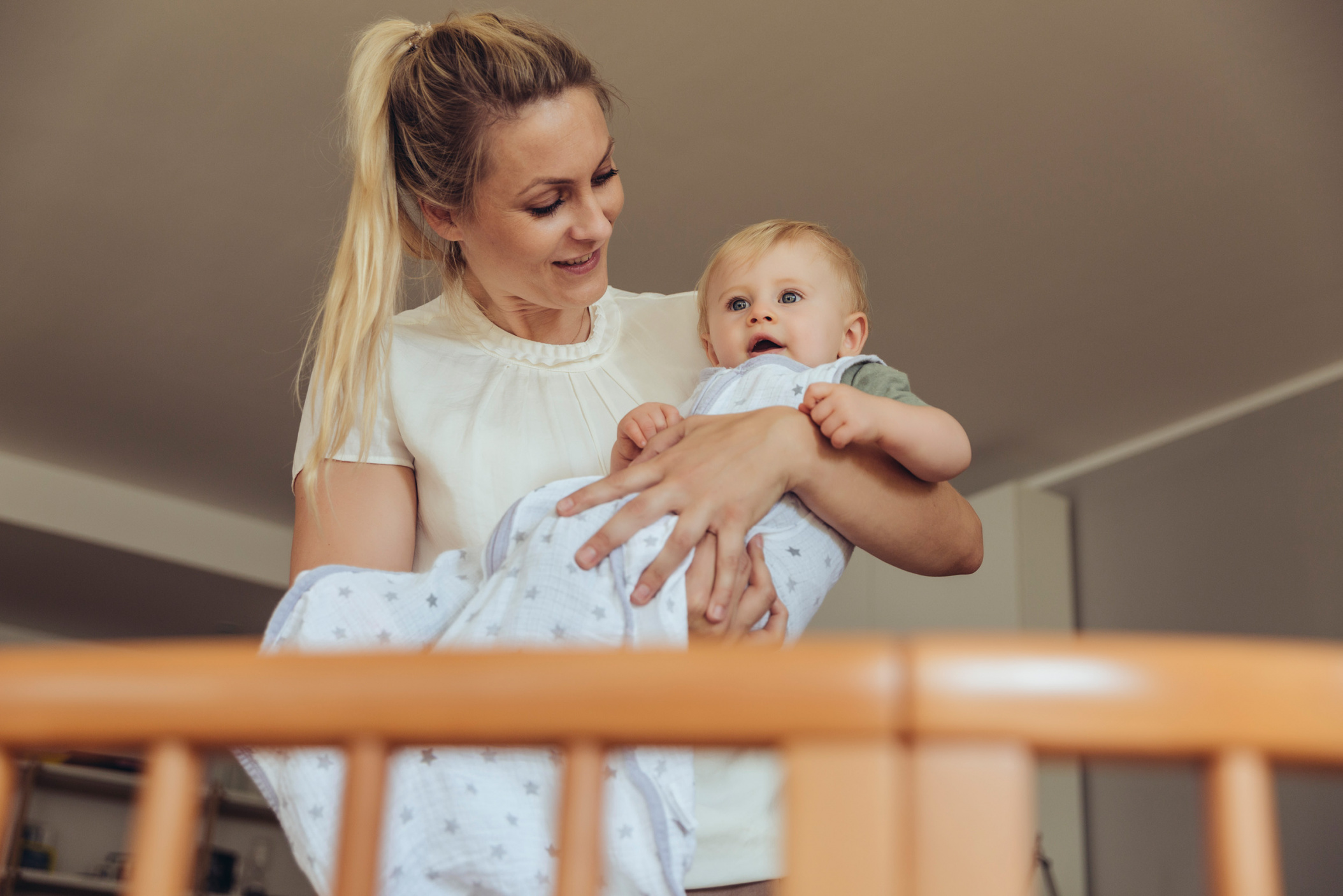 Mother putting baby (10 months) in its crib to sleep, Cologne, NRW, Germany
