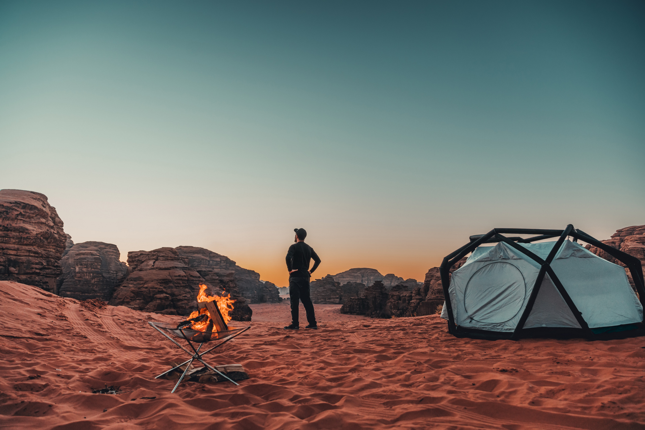 NEOM, SAUDI ARABIA – DECEMBER 10: Explorer with his camp fireplace set up by a tent overlooking Hisma Desert on December 10, 2022, in NEOM, Saudi Arabia.
