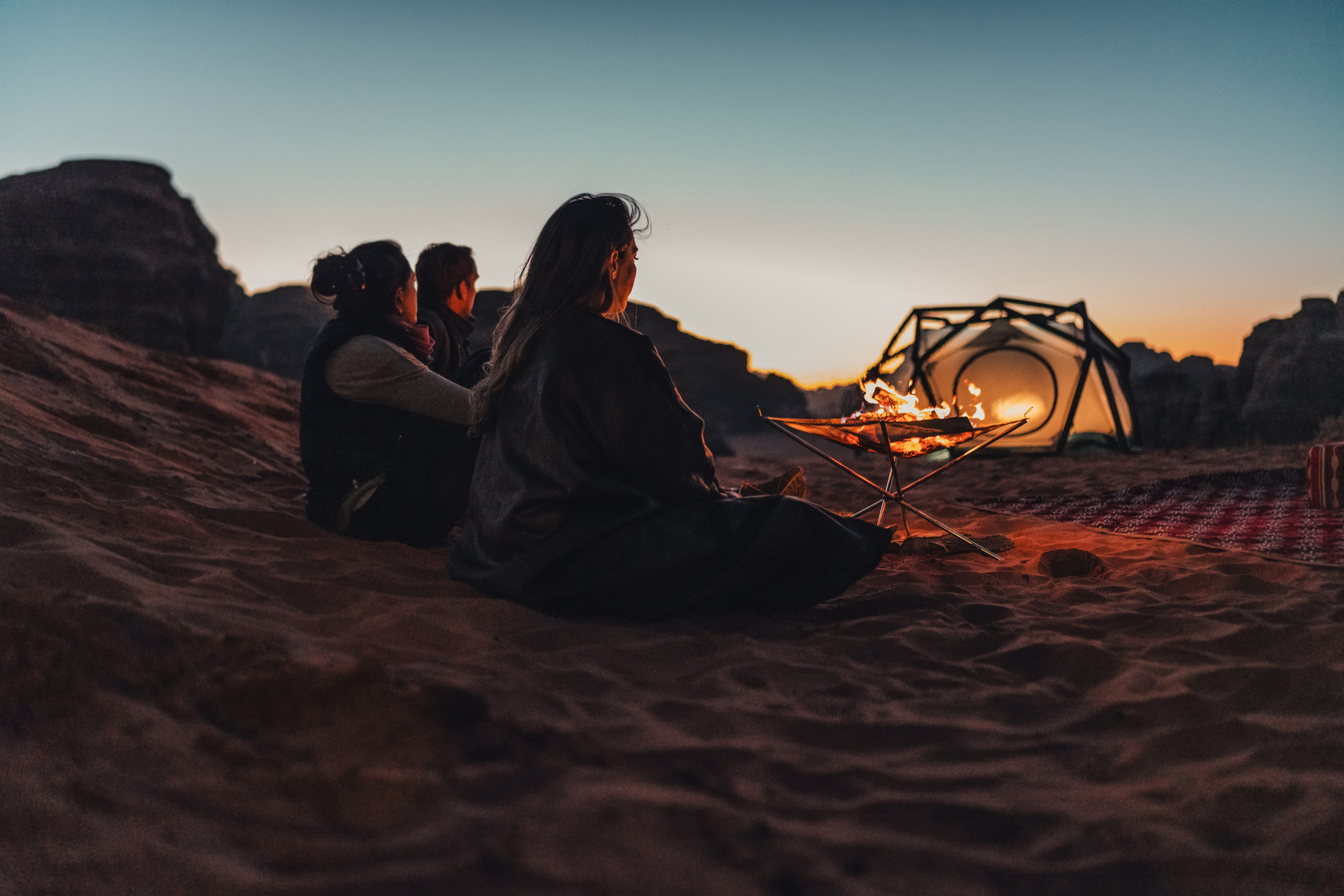 NEOM, SAUDI ARABIA – DECEMBER 10: Friends watching their fireplace next to a tent in Hisma Desert during sunset on December 10, 2022, in NEOM, Saudi Arabia.