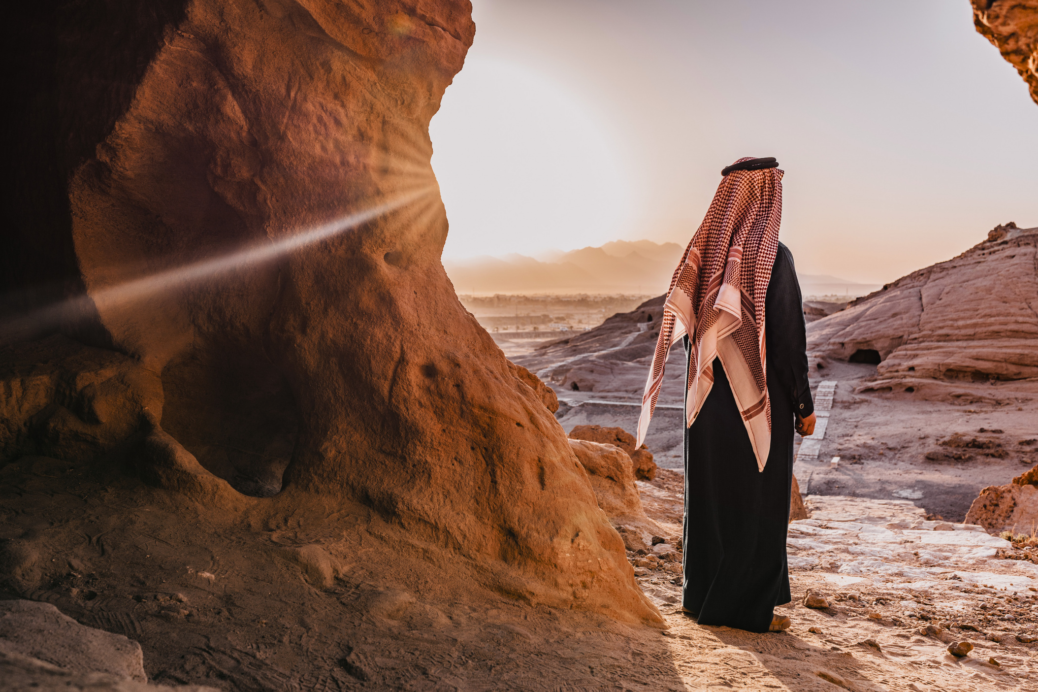 NEOM, SAUDI ARABIA – December 13: Saudi man watching sunrise from opening of ancient Tomb of Magha'er Shuaib on December 13,2022, in NEOM, Saudi Arabia.