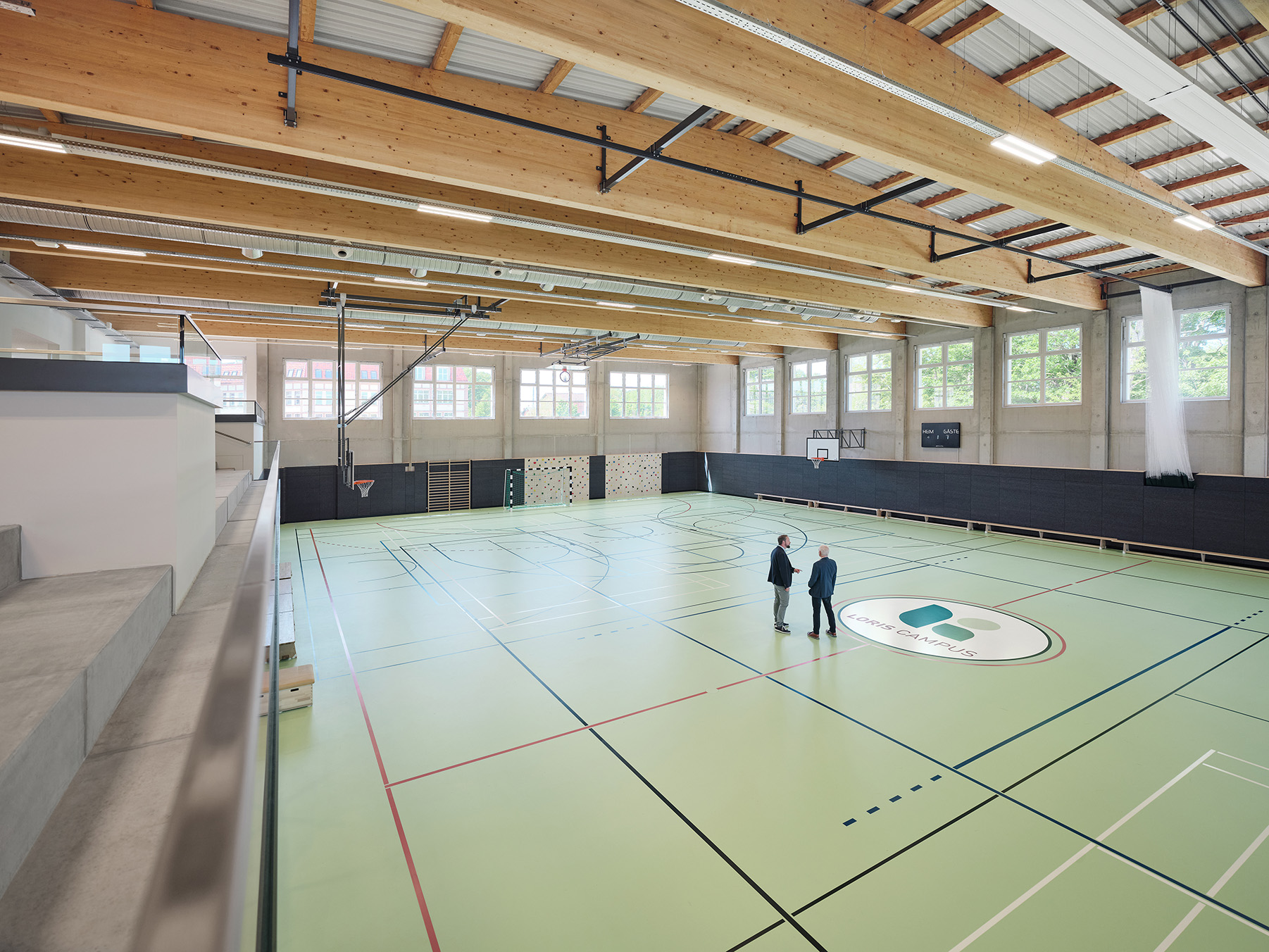 Modern school gymnasium with two people on green court by Mareen Fischinger
