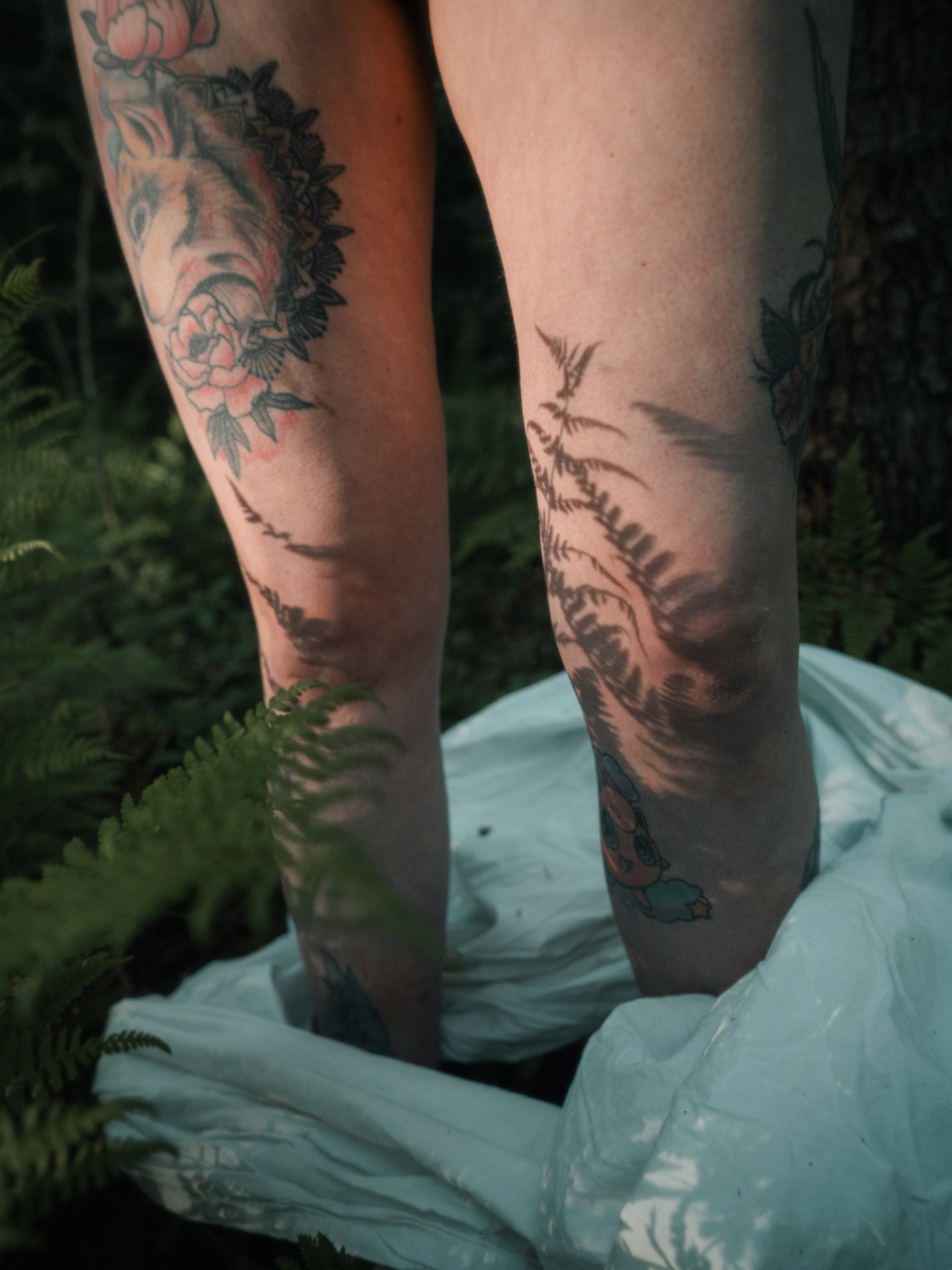 Tattooed legs with floral and fern designs in forest by Mareen Fischinger