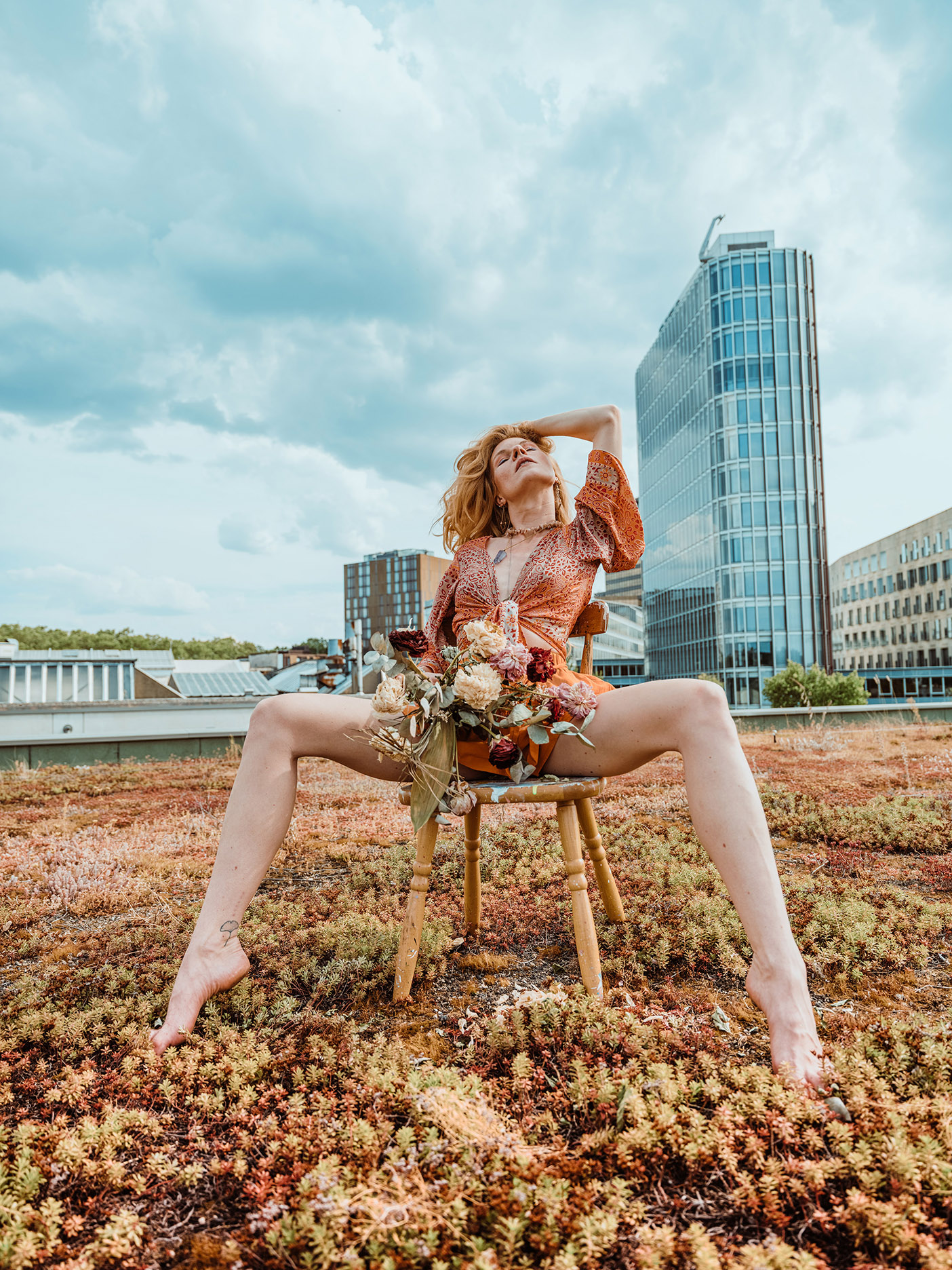 Woman in orange dress sitting on chair with flowers on rooftop