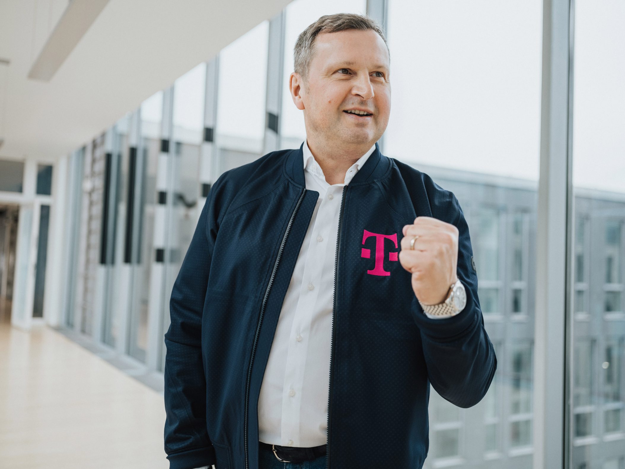 Mann in Telekom-Jacke lächelt in modernem Bürogebäude