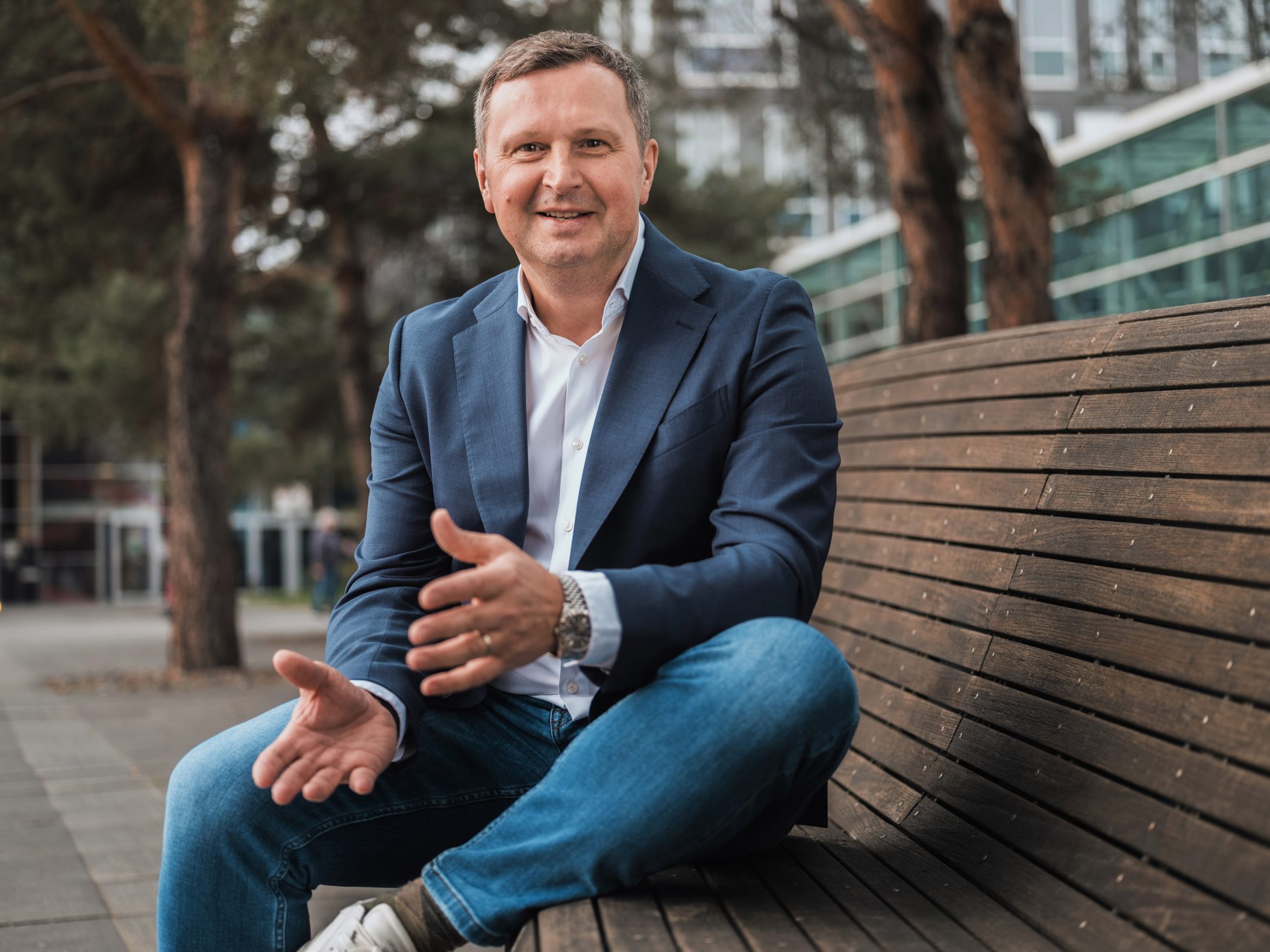 Lächelnder Mann im Blazer sitzt auf einer Parkbank