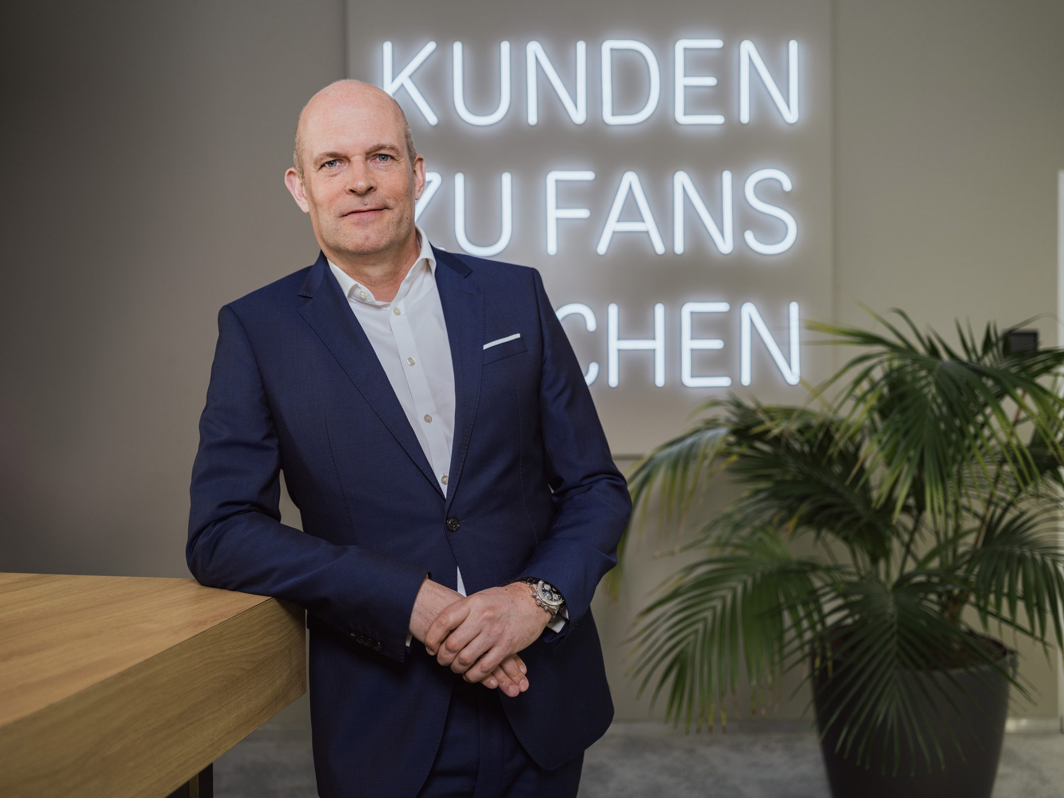 Geschäftsmann im Anzug vor Neonschrift Kunden zu Fans