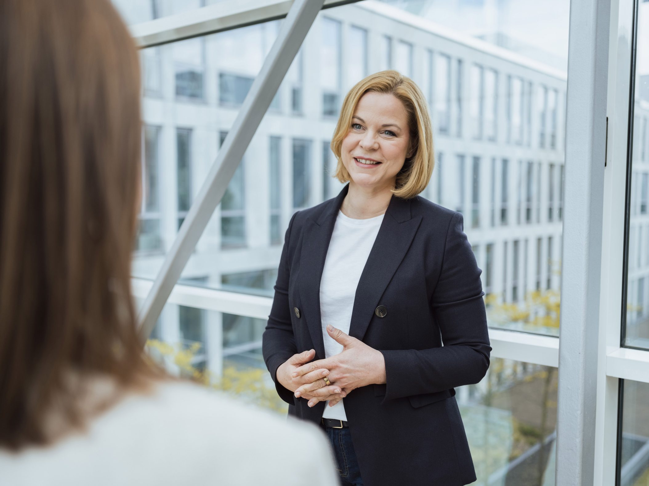 Geschäftsfrau im Blazer im Gespräch vor modernem Bürogebäude