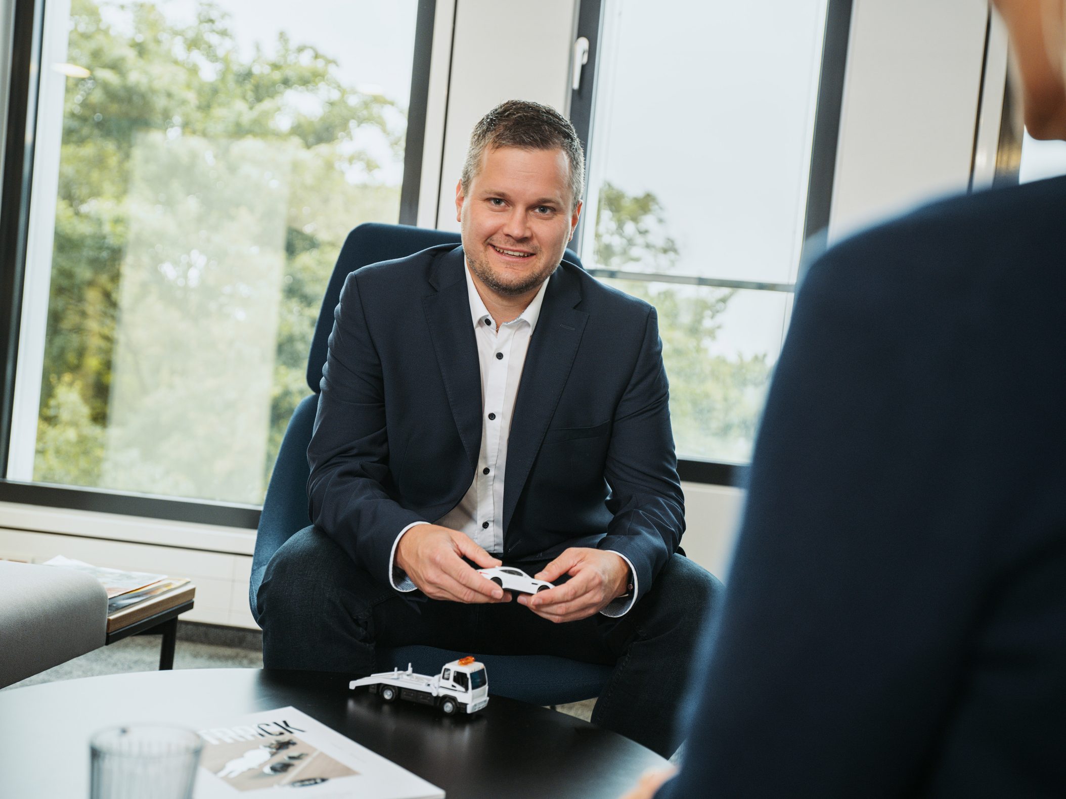 Geschäftsmann im Anzug hält Spielzeugauto bei Beratungsgespräch