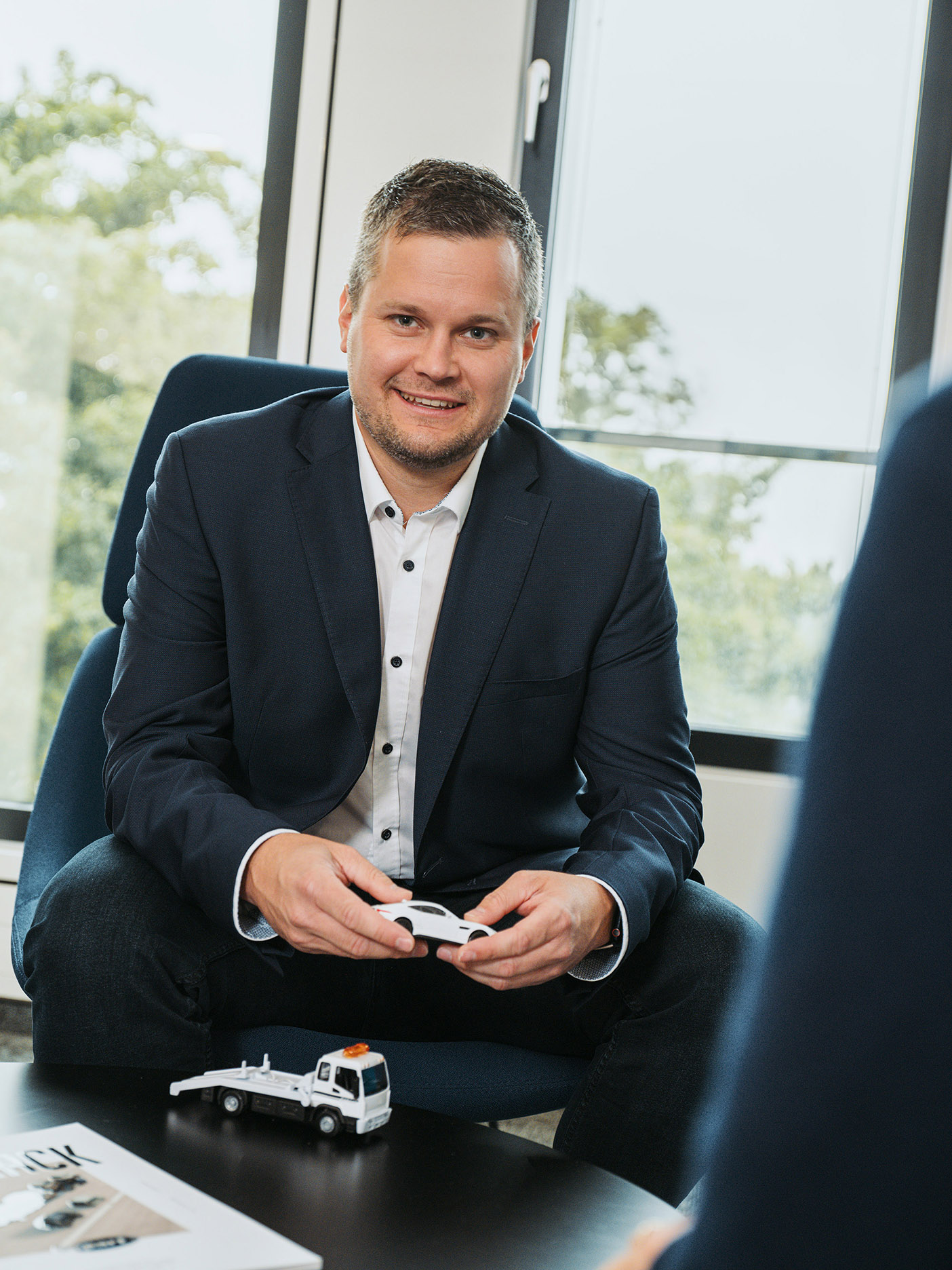 Lächelnder Geschäftsmann hält Modellauto im modernen Büro