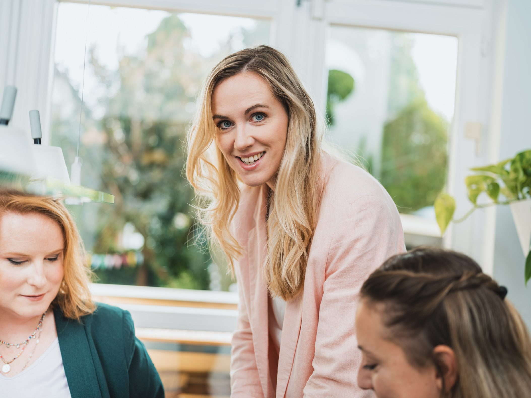 Smiling blonde woman leading a team meeting indoors by Mareen Fischinger