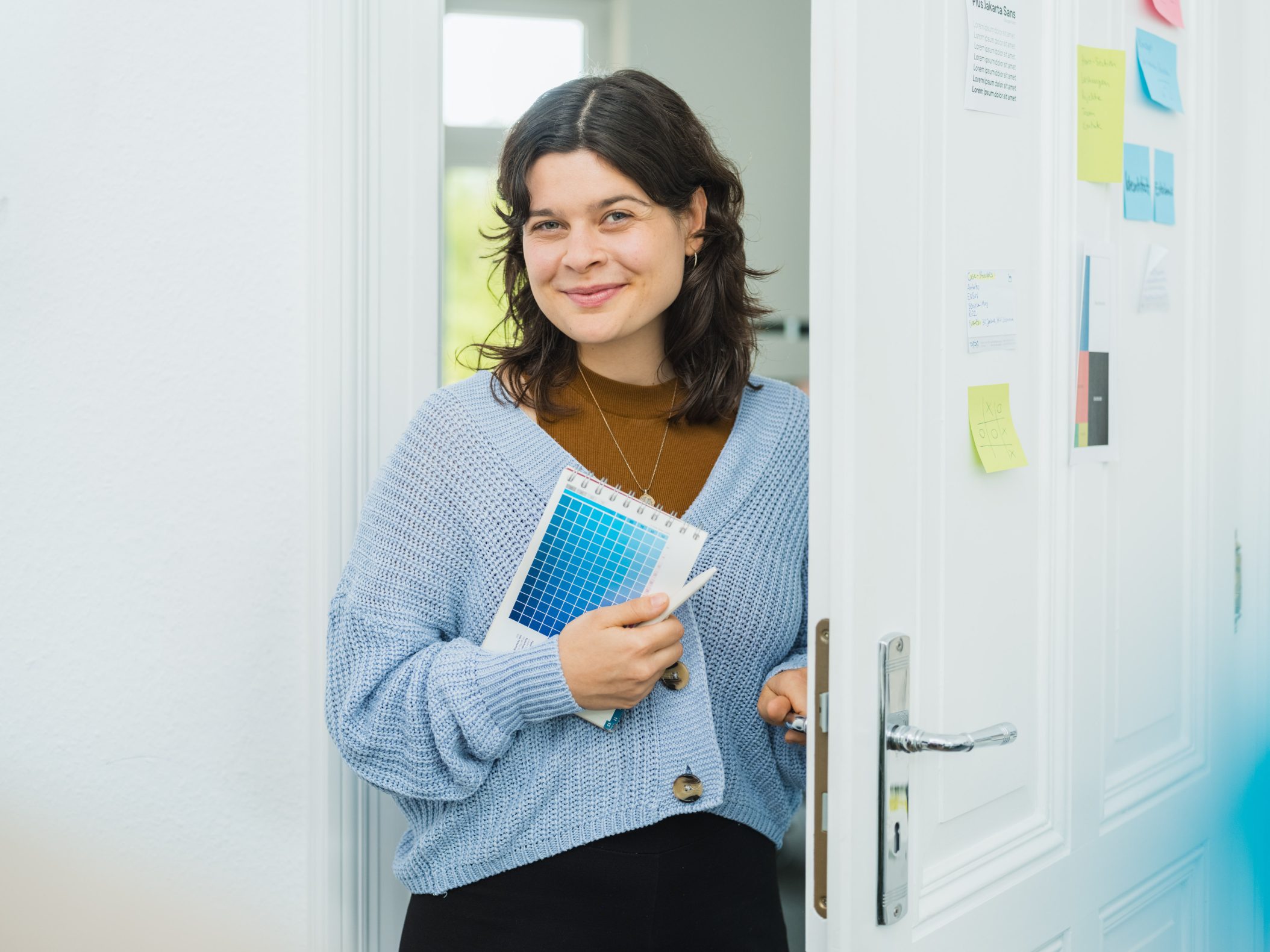 Smiling woman holding color swatches at office doorway by Mareen Fischinger