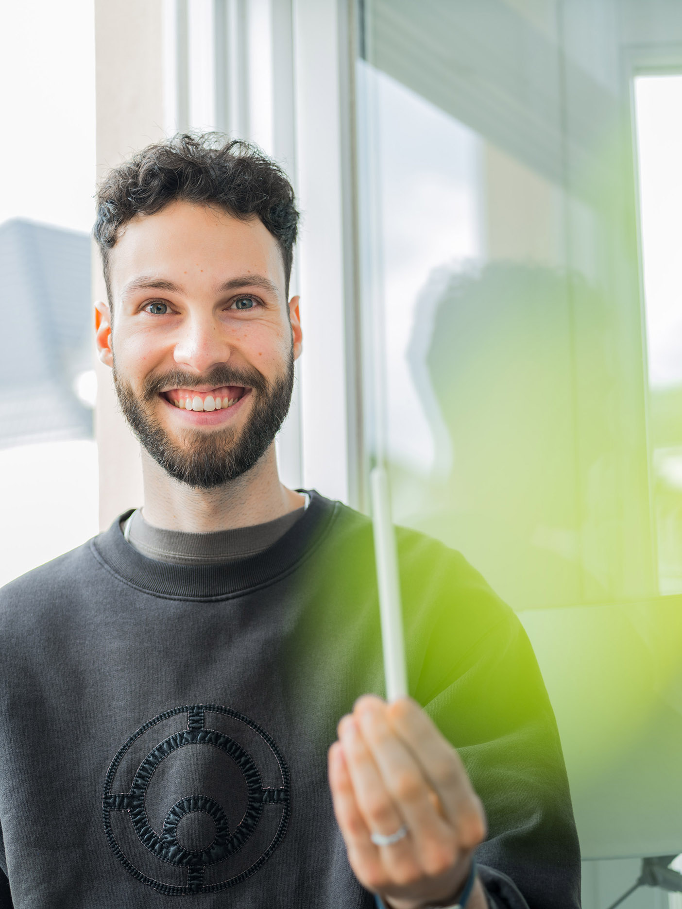 Smiling young man with beard holding a marker by window by Mareen Fischinger