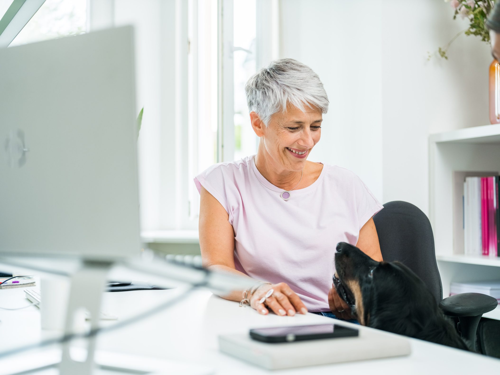 Smiling woman working at desk with her dog nearby by Mareen Fischinger