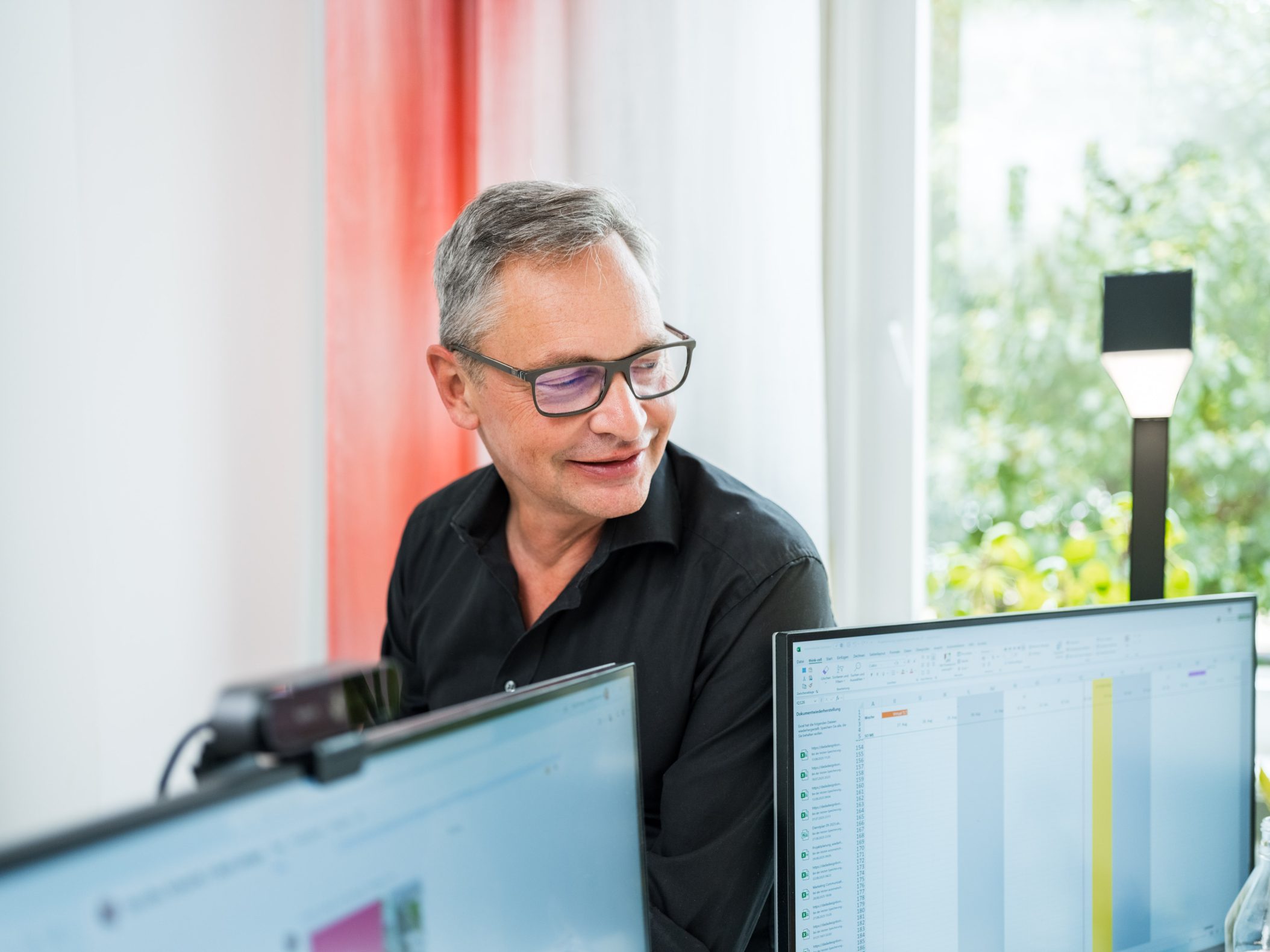 Middle-aged man with glasses working at dual computer monitors by Mareen Fischinger