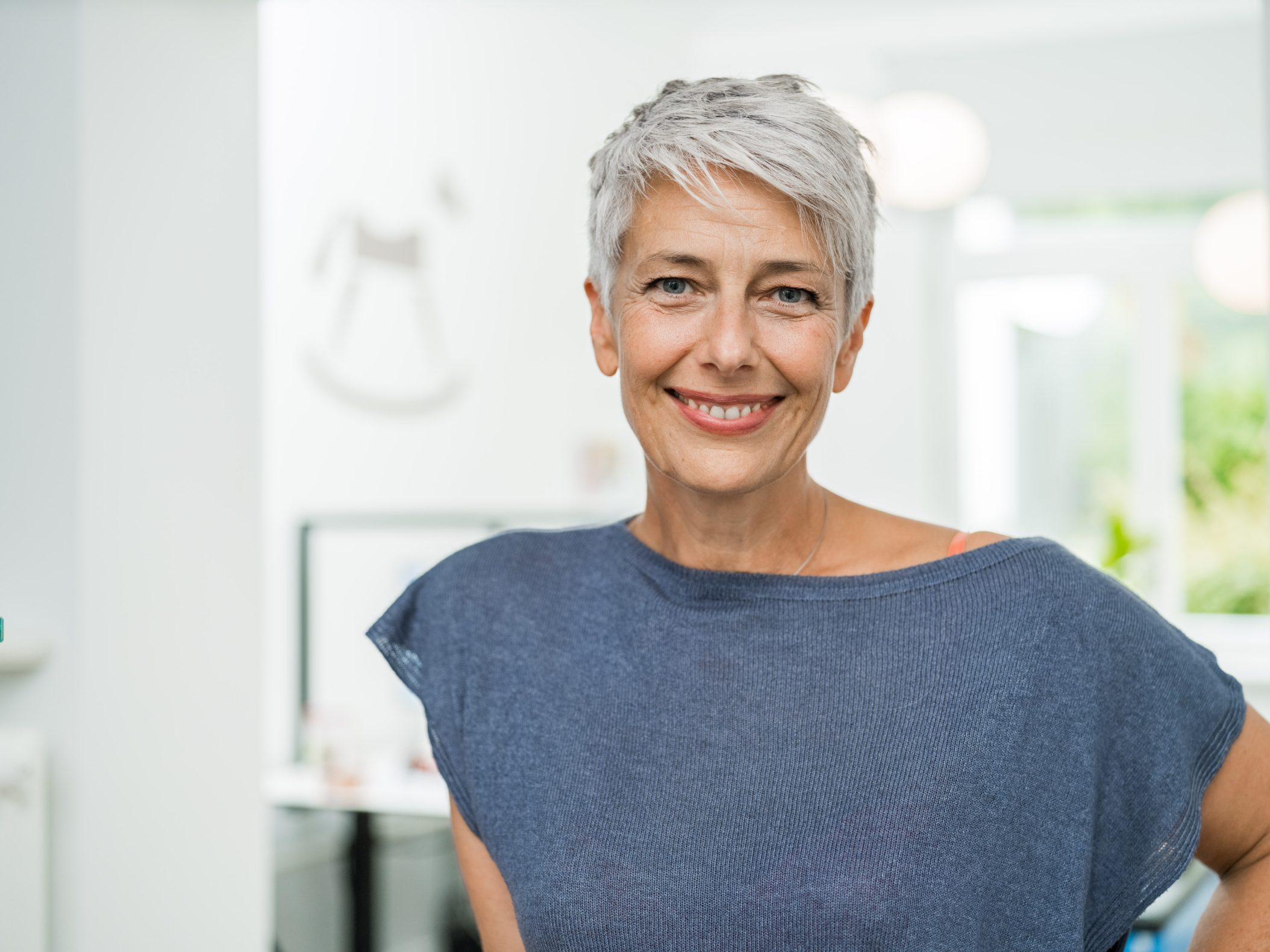 Smiling middle-aged woman with short gray hair indoors by Mareen Fischinger