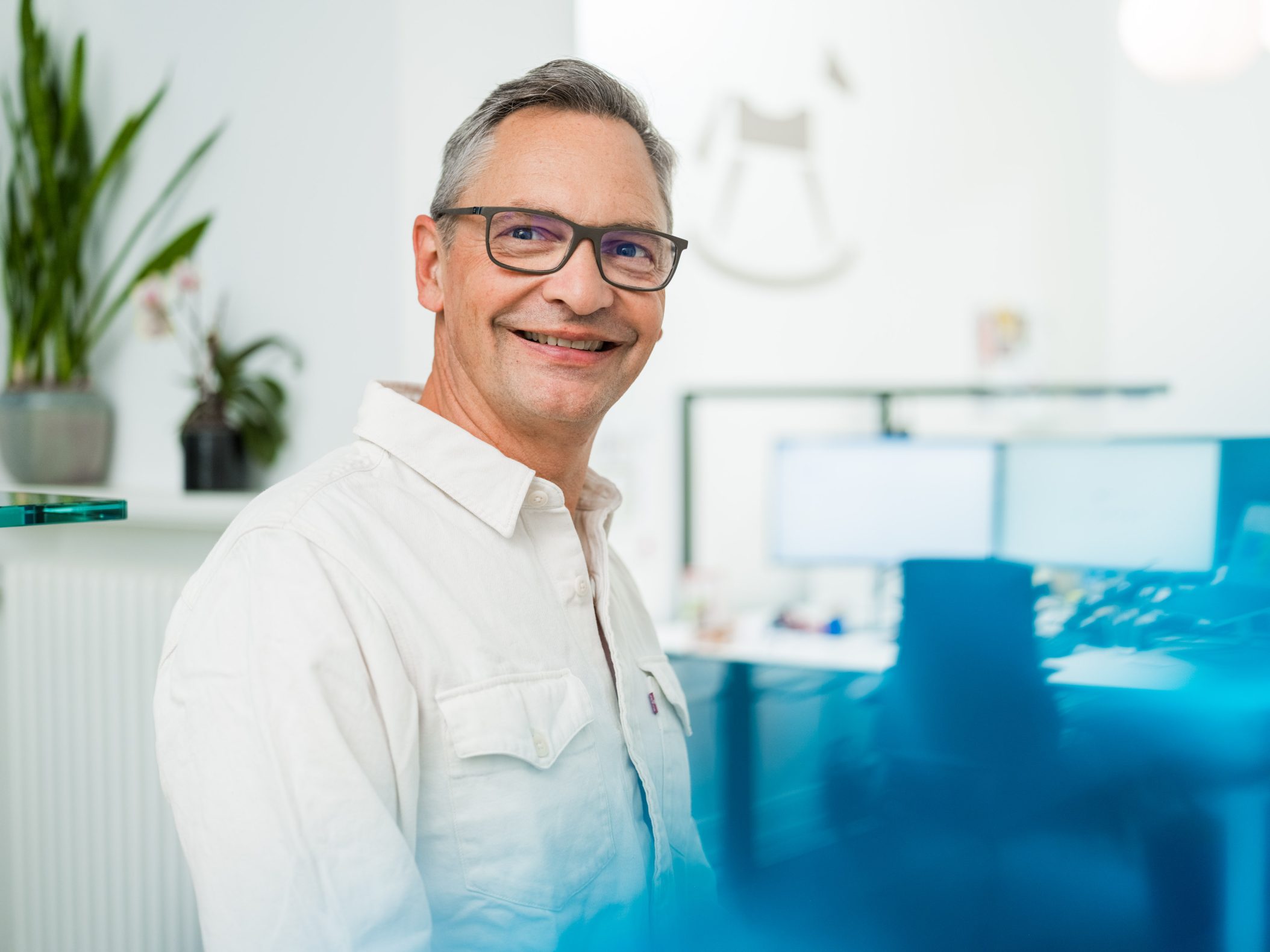 Smiling middle-aged man with glasses in modern office by Mareen Fischinger