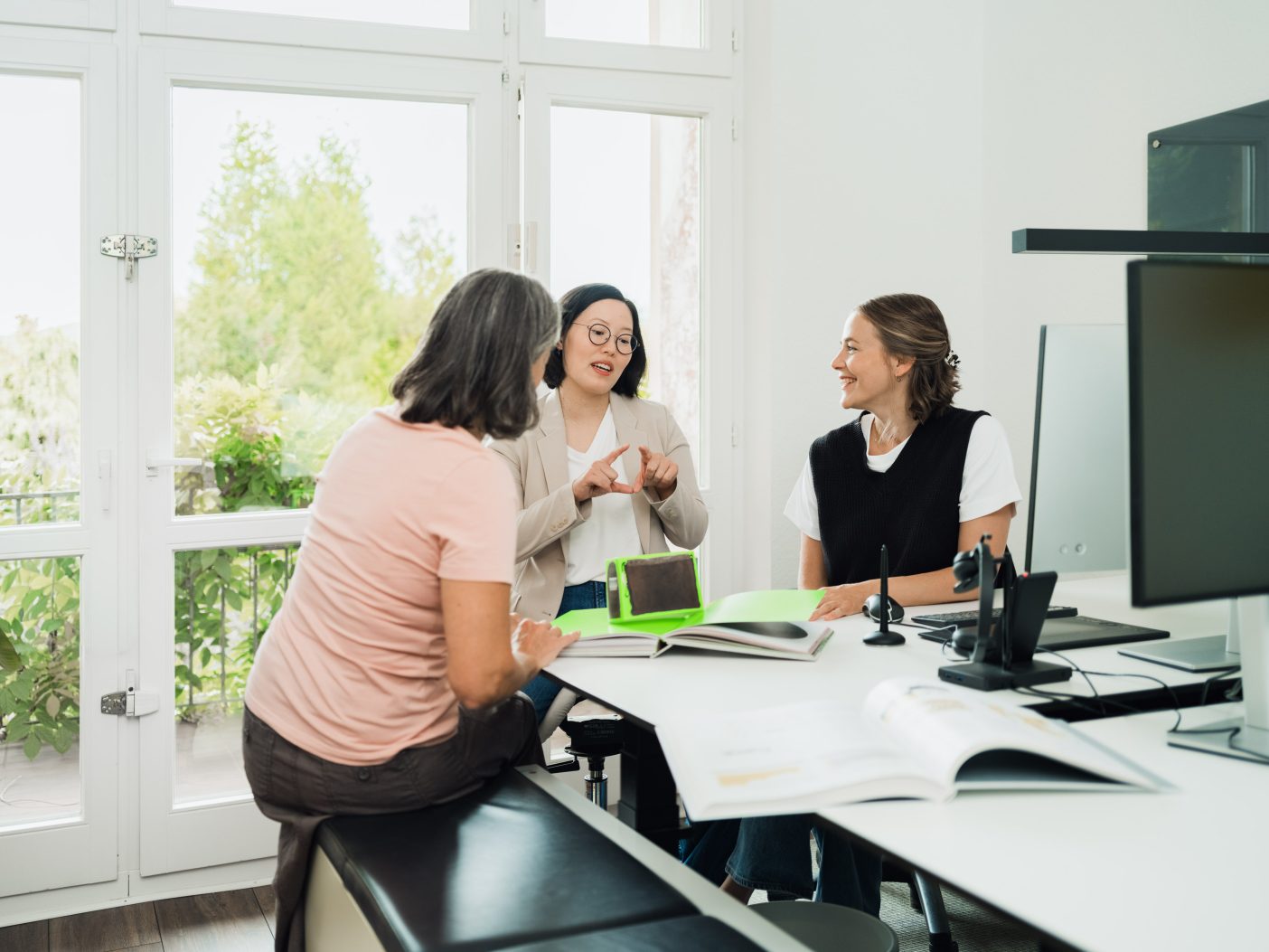 Three women collaborating and discussing work in bright office by Mareen Fischinger