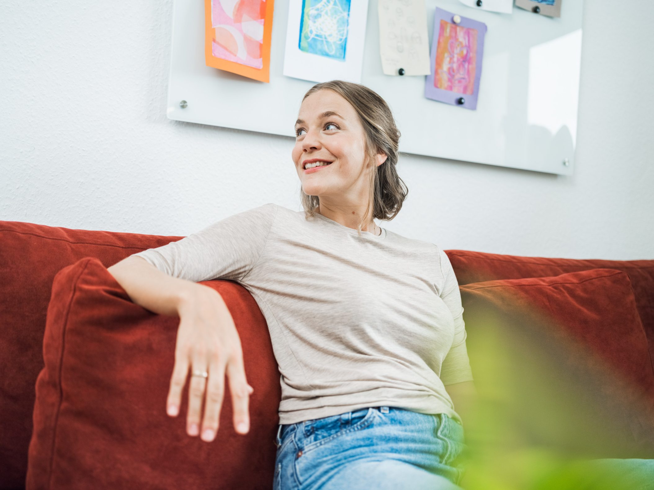 Smiling young woman relaxing on red sofa looking up by Mareen Fischinger